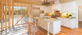 A "before and after" concept image of a kitchen remodel in Lansing, Michigan, showing the transition from bare wood framing to a finished custom kitchen with white cabinets and granite countertops. A "before and after" concept image of a kitchen remodel in Lansing, Michigan, showing the transition from bare wood framing to a finished custom kitchen with white cabinets and granite countertops.
